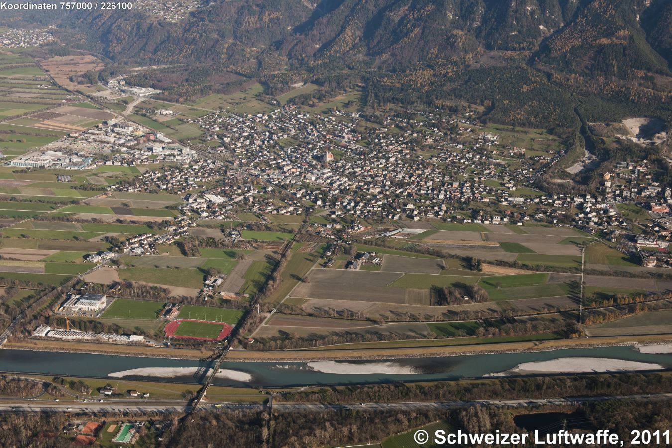 Schaan (FL) im Zentrum. Maiensäss nördlich davon (oberer Bildrand links): Planken. Dorf in der linken oberen Bildecke: Nendeln. Im Vordergrund am Rhein (links): Abenteuerspielplatz 'Dräggspatz'. Rechts im Bild: 'Möliholzröfi', eine Rüfe aus dem Drei Schwestern-Gebiet.
